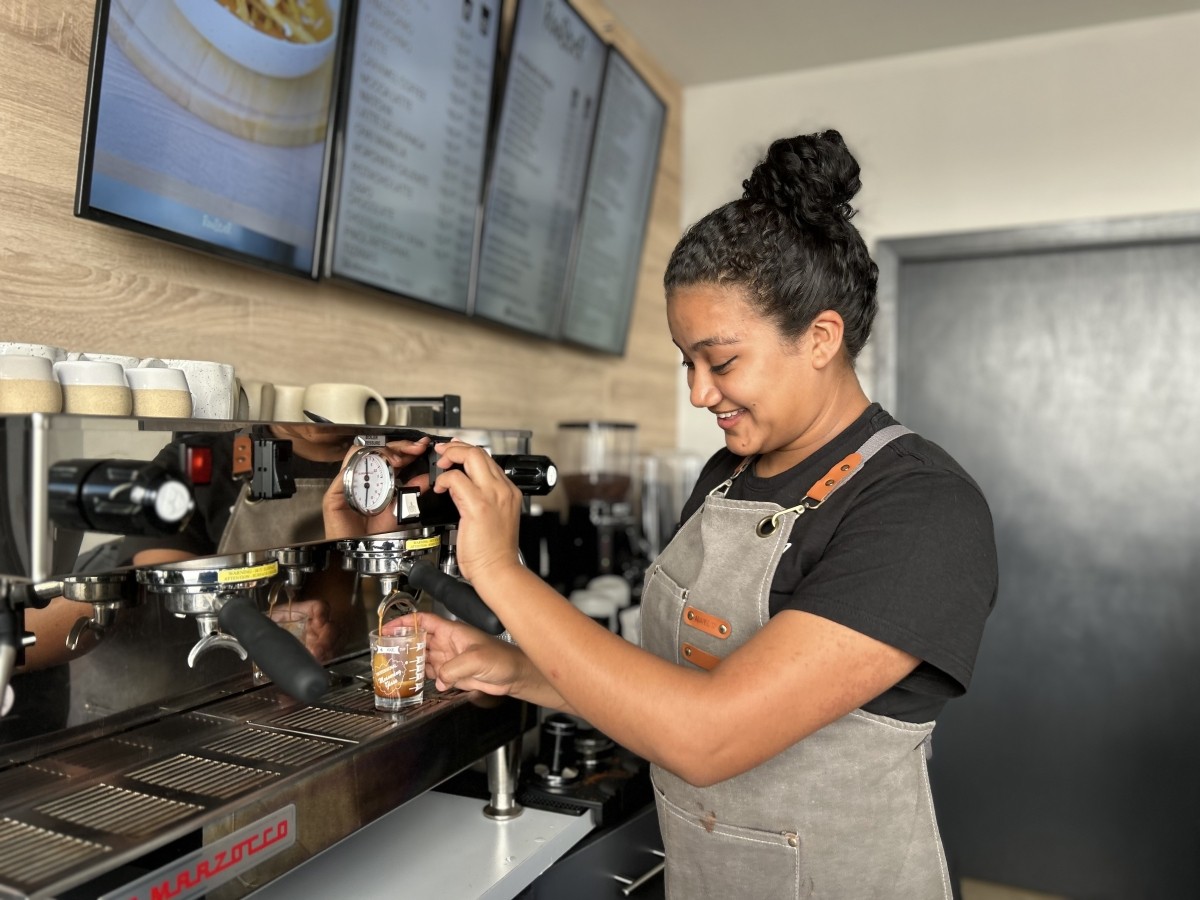 A young woman makes a coffee drink in a cafe.