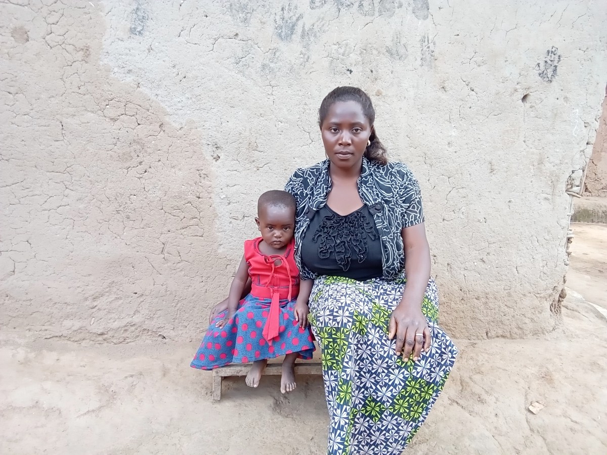 A mother and her young daughter sit on a small bench in front of a wall