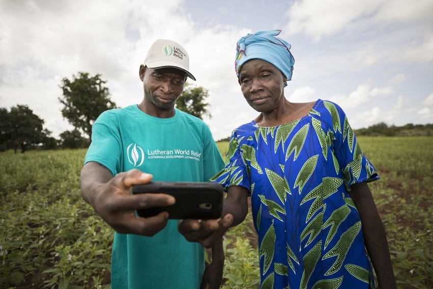 A man and a woman stand in a field and look at a phone