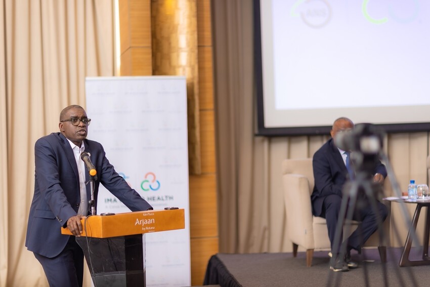 A main in a suit gives a speech at a podium with an IMA World Health banner behind him