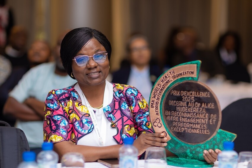 A woman smiles and sits at a table while holding a trophy