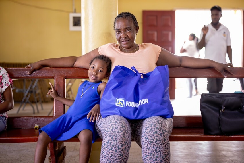 A mom and daughter sit on a bench holding a food package