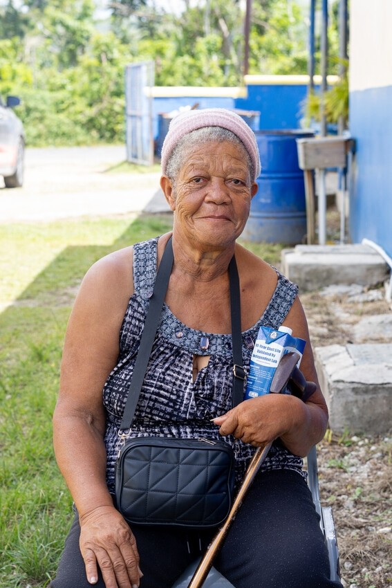 An older woman sits outside on a chair, holder her cane.