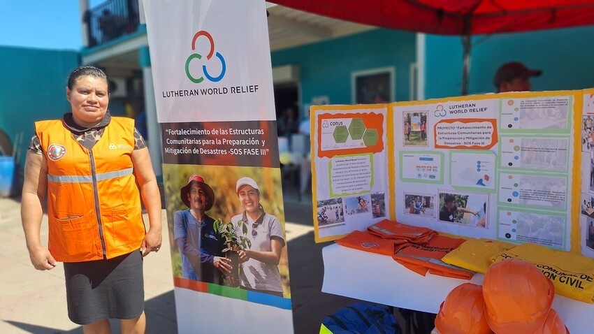 A woman in an orange safety vest stands in front of an outdoor booth with emergency preparedness information
