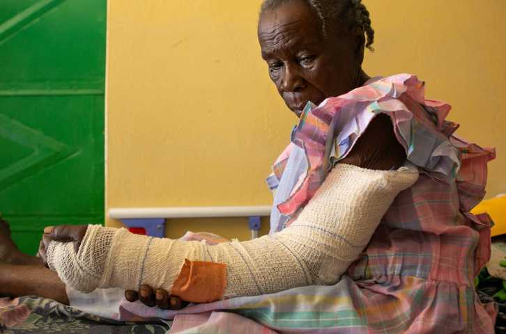 Une femme haïtienne regarde son bras, qui est enveloppé dans un bandage.