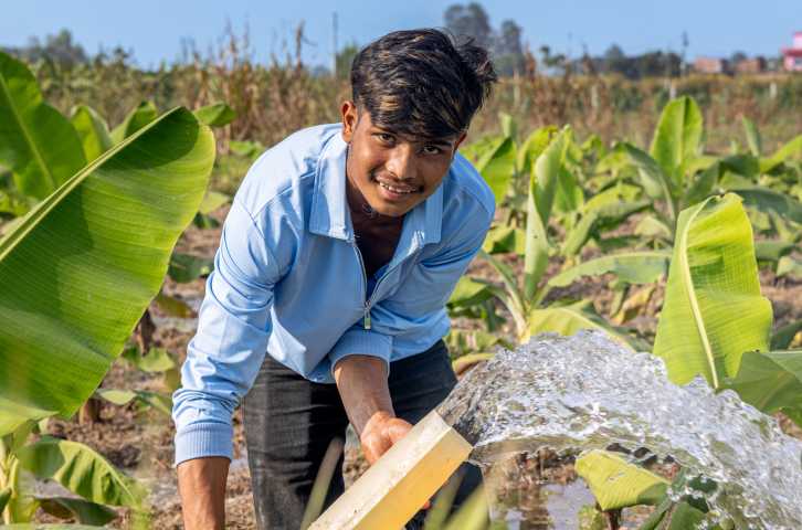 A young Nepali farmer holds a hose with streaming water in a banana field