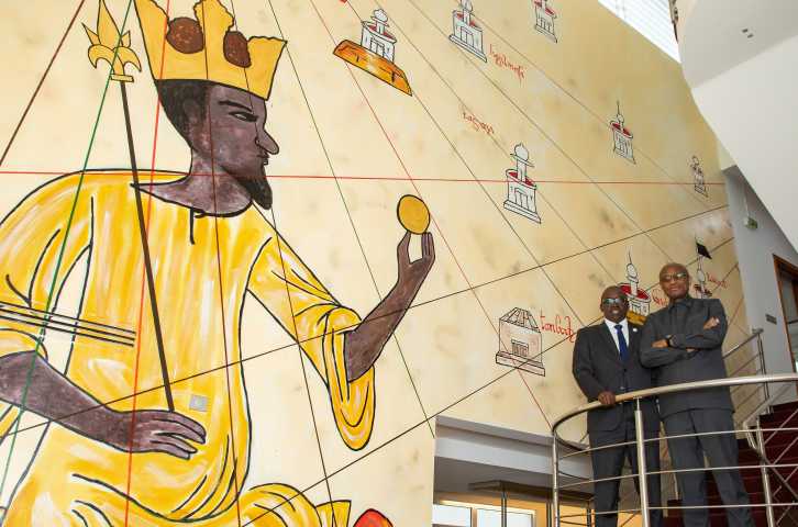 Mahmoud Bah and El-Hassana Kaba stand on stairwell in MANSA BANK next to iconic mural.