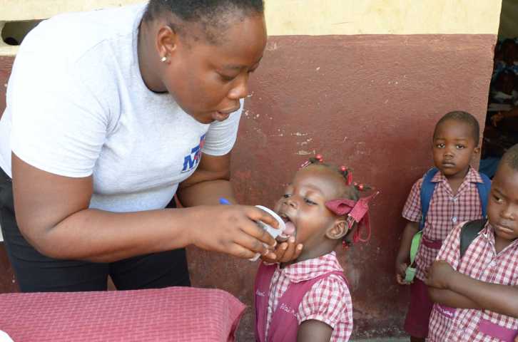 A community health worker gives medicine to prevent neglected tropical diseases to a schoolgirl in Haiti.