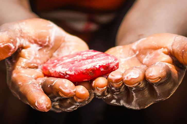 Las manos enjabonadas de un niño están extendidas sosteniendo una pastilla de jabón roja