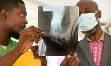 Dr  Dummond Done Doulo, left, and hospital director, Dr  Pierre Robert Azor, and examine an X-ray of the crushed foot of a victim of a 7 2 magnitude quake that devastated the region on August 14, at the St  Antoine Hospital in Jeremie, in the Grand Anse department of Haiti, August 23, 2021  (Photo by Allison Shelley for LWR Corus)