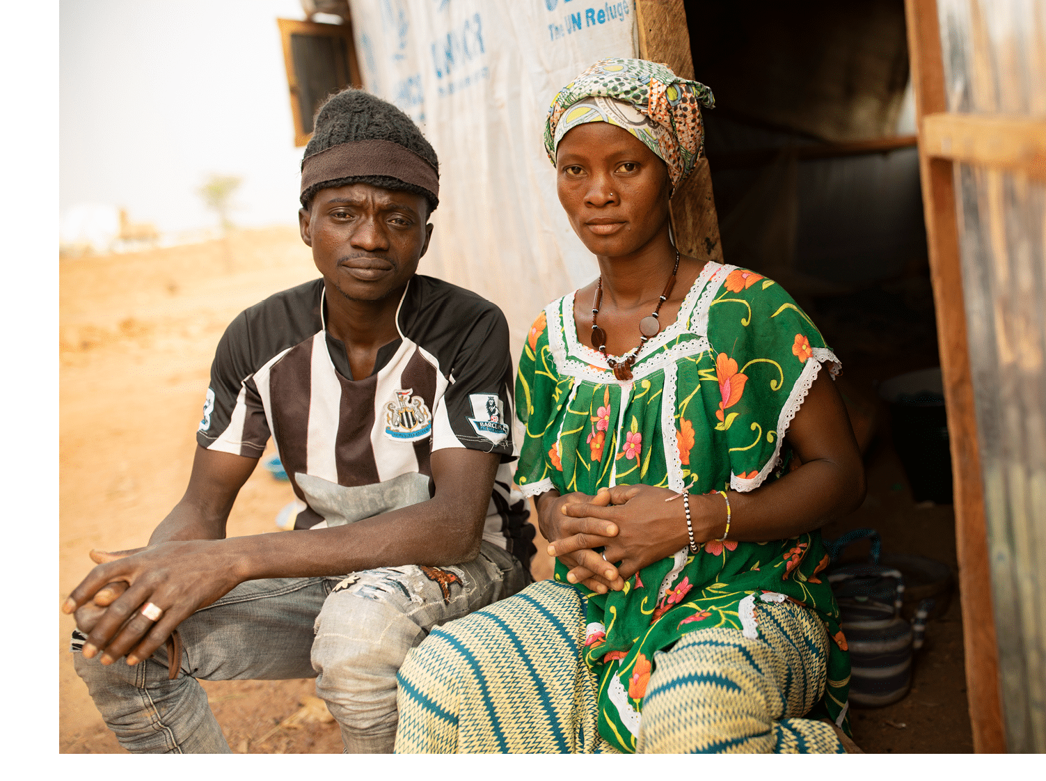 Adama Guindo (30, L) sits outside his family s shelter in Nouna, Burkina Faso, with his wife, Traore Jeneba (20, R)  His family fled violence and insecurity following the abduction of his father in the northeast of the country and now faces hunger and hardship here  Jeneba is also expecting a child and thus needs more nutritious food than most people  Sahel 2021 Crisis; Kossi Province, Burkina Faso   Feb 19, 2021  Photo by Jake Lyell 